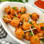 Side angle of sausage bites in a bowl with toothpicks and fresh parsley.