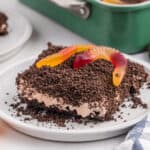 A Cool Whip Desserts favorite, this treat features crushed chocolate cookies, creamy filling, and colorful gummy worms, all served on a white plate with a baking dish and whole cookies in the background.