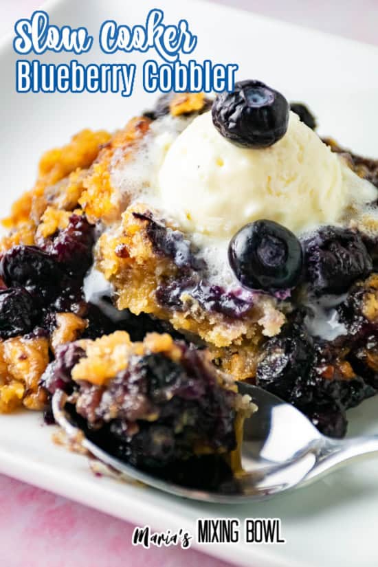 A close-up of blueberry cobbler topped with a scoop of vanilla ice cream, melting slightly, served on a white plate with a spoon. Text reads Slow Cooker Blueberry Cobbler and Marias Mixing Bowl.