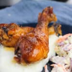 Two glazed chicken drumsticks served on a bed of mashed potatoes, accompanied by coleslaw with shredded carrots and cabbage, presented on a dark plate—perfect for 4th of July Chicken Recipes.
