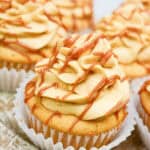 Close-up of dulce de leche cupcakes with swirled caramel-colored frosting, drizzled with caramel sauce, arranged on a rustic wooden plate.