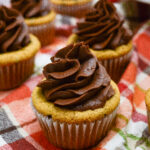 A close-up of cupcakes with swirled chocolate frosting on top, placed on a colorful plaid cloth, perfect for anyone wondering how to keep cupcakes moist and delicious.