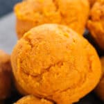 Close-up of several golden-orange pumpkin muffins with a slightly rough texture, stacked on top of each other—similar in color and simplicity to 2 ingredient pumpkin cookies.
