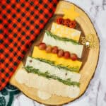 Christmas tree-shaped cheese board with layers of sliced cheese, grapes, and crackers, garnished with rosemary.