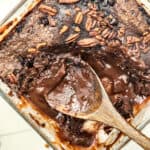 A glass baking dish filled with gooey chocolate lava cake, one of the ultimate winter cakes, topped with chopped pecans. A wooden spoon scoops out the rich, melted chocolate center, highlighting the dessert’s moist texture.