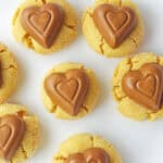 Seven peanut butter cookies topped with heart-shaped chocolates on a white plate.