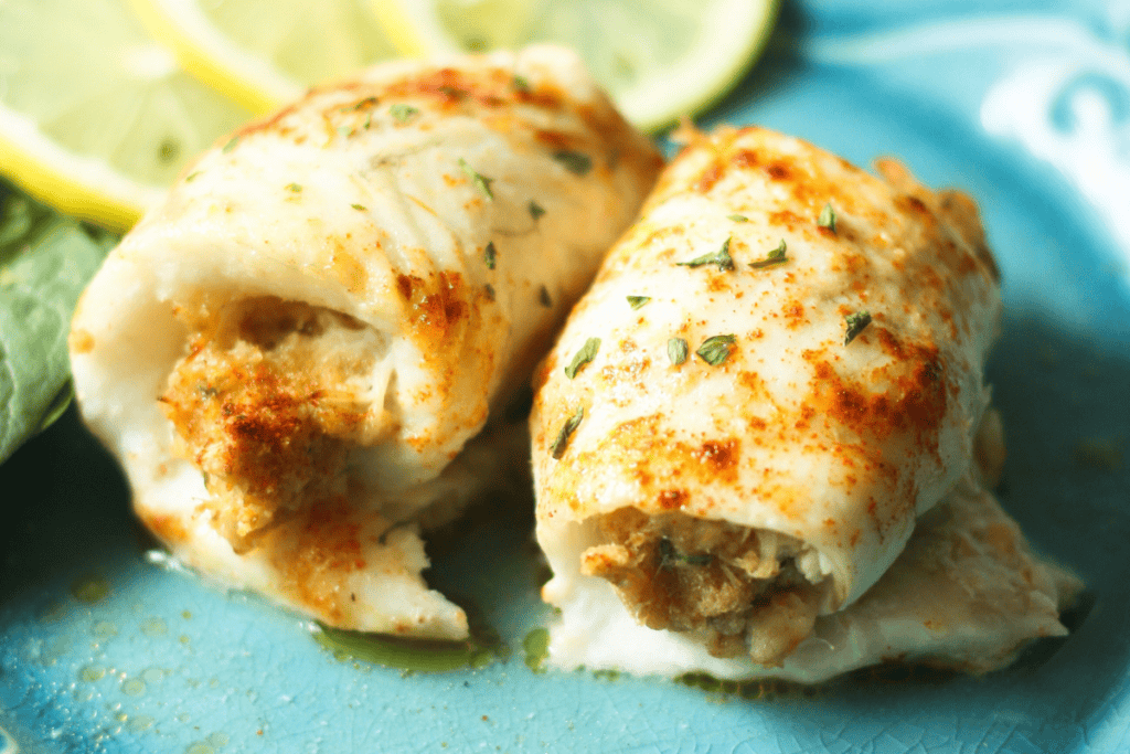 Two pieces of crab stuffed flounder on a blue plate with lemon slices.