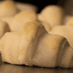 A close-up of golden, freshly baked crescent rolls in air fryer with a soft, flaky texture, arranged together on a baking tray.