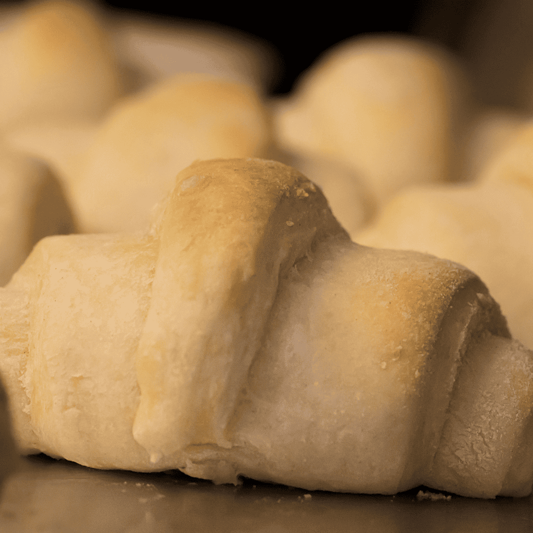 A close-up of golden, freshly baked crescent rolls in air fryer with a soft, flaky texture, arranged together on a baking tray.