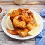 A white plate with crispy breaded shrimp and lemon wedges, next to a small bowl of cocktail sauce on a wooden table with a blue cloth—perfect for Valentine’s Day Dinner Ideas.