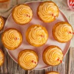 Frosted cupcakes arranged on a pink plate with striped straws inserted.