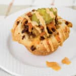 A savory muffin topped with ground meat, melted cheese, two pickle slices, and drizzled with a creamy orange sauce makes one of the best easy appetizers for a party, beautifully served on a white plate.