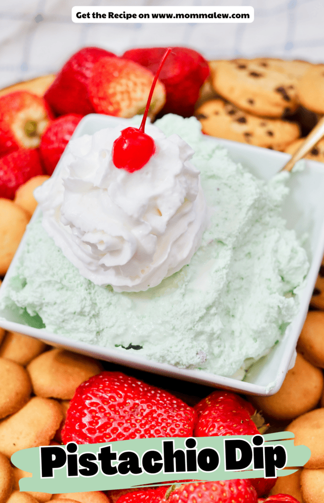 A bowl of creamy pistachio dip topped with whipped cream and a cherry, surrounded by strawberries, vanilla wafers, and cookies. Text reads Pistachio Dip and Get the Recipe on www.mommalew.com.