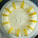 A top-down view of a creamy lemon pie, one of the classic lemon desserts, topped with swirls of whipped cream and garnished with lemon slices around the edge, set on a white plate.