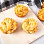 Four golden-brown crab stuffed cheddar bay biscuits are arranged on a white cutting board, with a black and white checkered cloth in the background. The muffins appear fluffy with melted cheese visible on top.