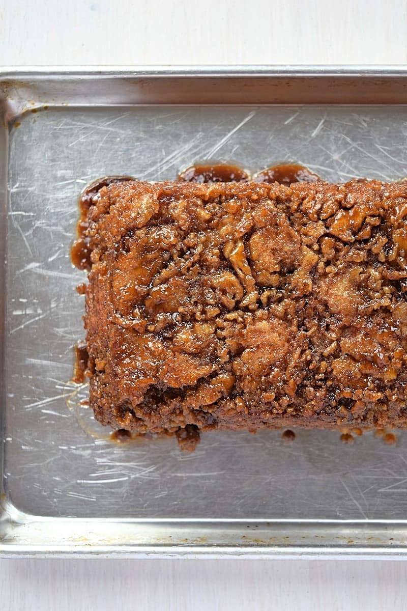 A loaf of cinnamon swirl bread with a crumbly, caramelized topping sits on a metal baking tray, viewed from above. This golden brown treat is a delicious example of easy loaf pan recipes for homemade baking lovers.