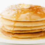 A close-up of pancakes stacked and covered in syrup with a pat of butter on top.