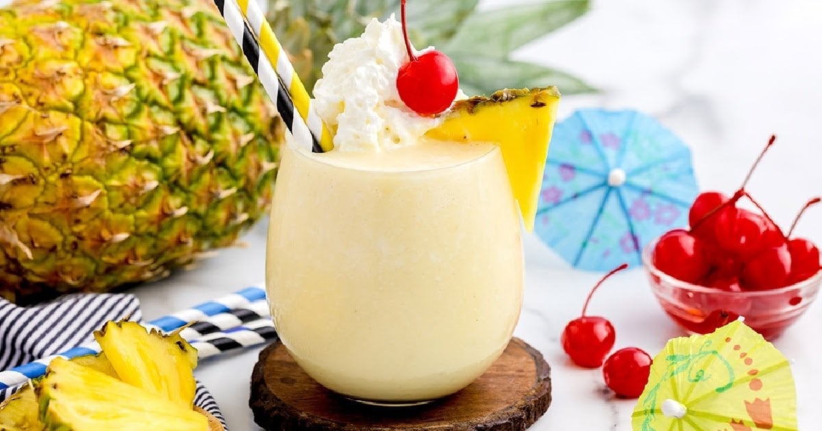 Pineapple drink in a round glass topped with whipped cream, a cherry, and a pineapple slice.