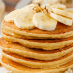 A stack of pancakes topped with banana slices and a drizzle of sauce on a speckled plate.