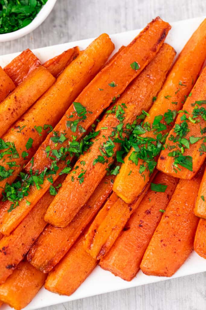 Baked Carrots with Brown Sugar glazed and roasted, arranged on a white plate and garnished with chopped fresh parsley.