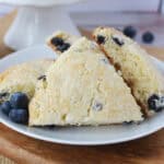 A white plate with blueberry scones and a few fresh blueberries on the side.