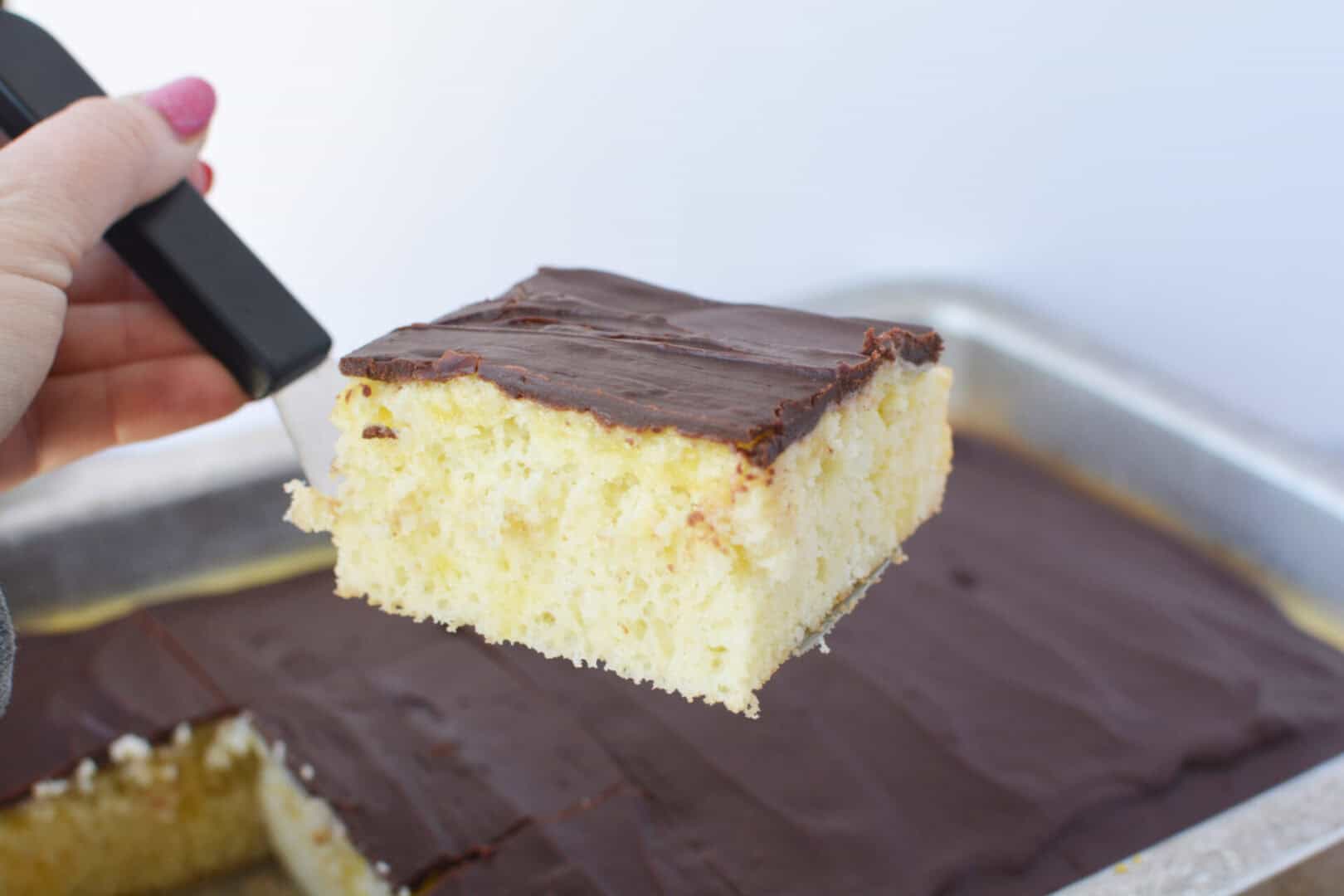 A slice of chocolate eclair poke cake being lifted from the pan with a spatula.