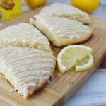 Lemon scones with icing on a wooden board, lemon slices and whole lemons nearby.