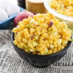 A black bowl filled with macaroni salad sitting on newspaper print cloth