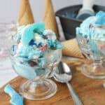 Two glass bowls filled with shark-themed ice cream, topped with gummy sharks on a wooden board.