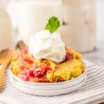 A bowl of cherry pineapple dump cake topped with whipped cream and mint on a striped cloth.