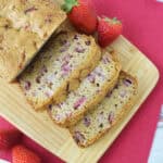 Overhead view of sliced strawberry bread on a wooden board with whole strawberries.