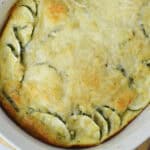 Golden-brown zucchini bake with melted cheese in a white oval baking dish.