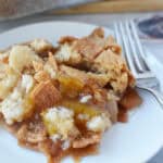 A serving of peach cobbler with a crumbly topping and pieces of Cinnamon Toast Crunch Dump Cake on a white plate, accompanied by a fork.