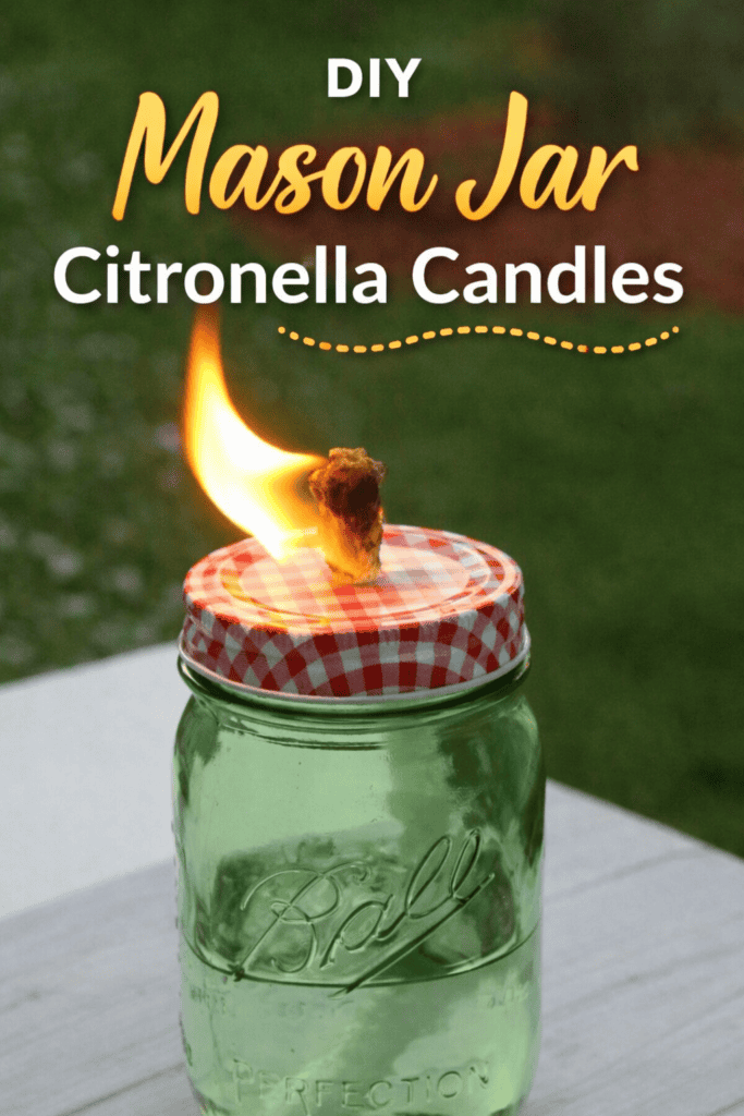 A green Ball mason jar with a red and white checkered lid is used as a Mason Jar Citronella Candle, its flame gently burning. Text above reads: DIY Mason Jar Citronella Candles. The grassy background is softly blurred.