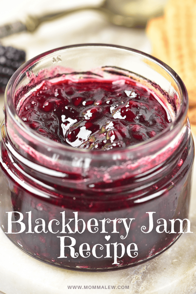 An open glass jar filled with blackberry jam sits on a white surface, showcasing the rich color of this homemade blackberry jam recipe. The text “Blackberry Jam Recipe” is written over the photo, with the website “www.mommaleew.com” below.