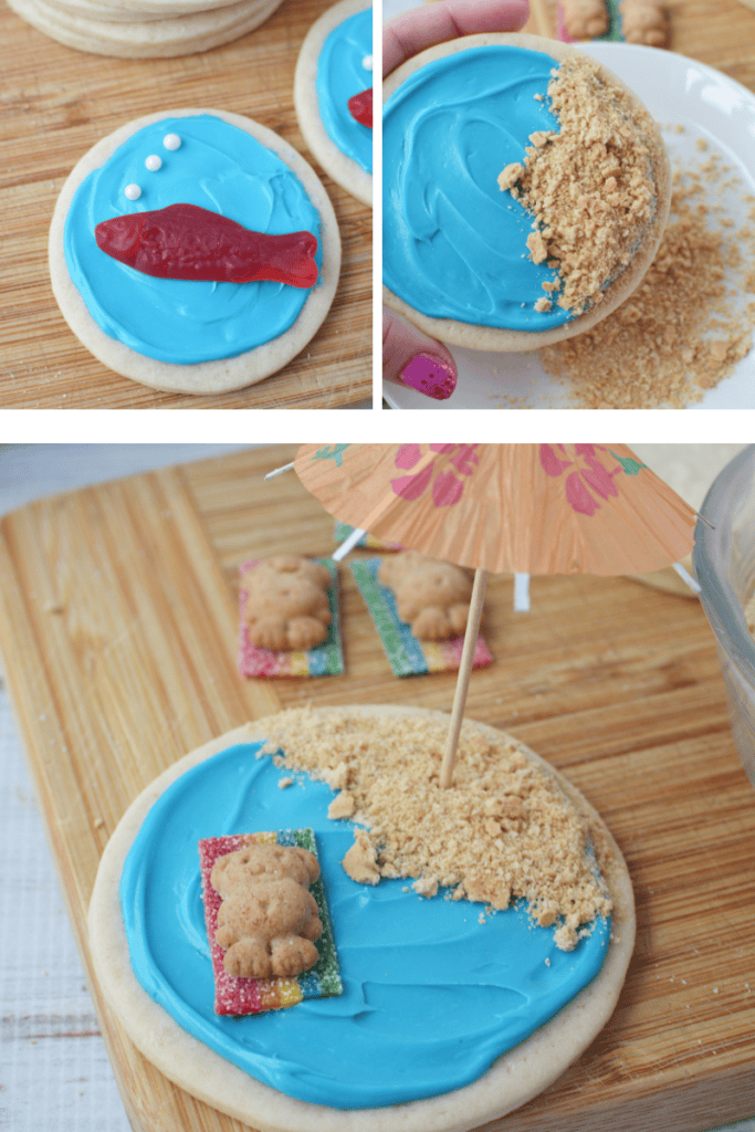 Beach sugar cookies decorated with blue icing, crushed graham cracker sand, a candy fish, and a teddy-shaped cookie on a candy “towel,” under a mini paper umbrella—they create an adorable beach scene treat.