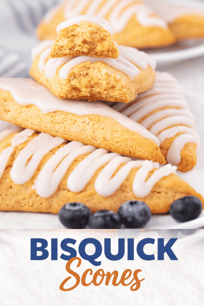 Triangular Bisquick scones drizzled with white icing are stacked on a plate, with one broken scone on top. Fresh blueberries are in the foreground. Text reads BISQUICK Scones.