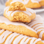 Close-up of golden-brown, triangular bisquick scones with white icing drizzled on top. One scone is broken in half, revealing its soft, crumbly interior, and rests atop a whole scone.