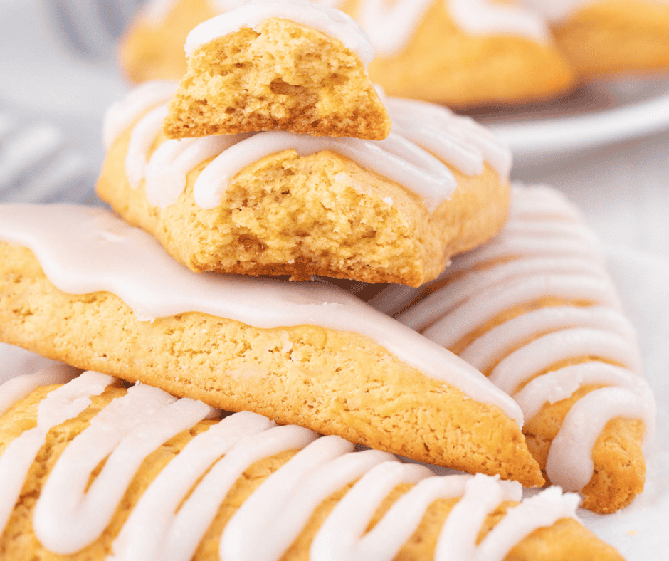Close-up of golden-brown, triangular bisquick scones with white icing drizzled on top. One scone is broken in half, revealing its soft, crumbly interior, and rests atop a whole scone.