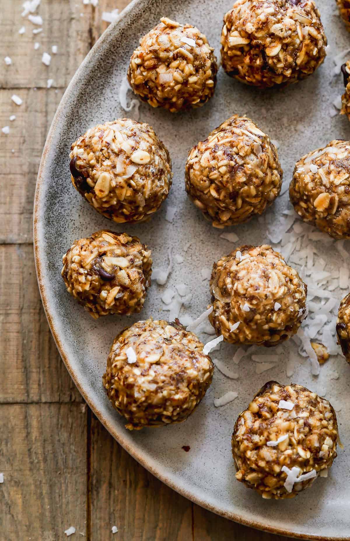 A ceramic plate holds several round oatmeal energy balls with shredded coconut sprinkled around them, placed on a rustic wooden surface.