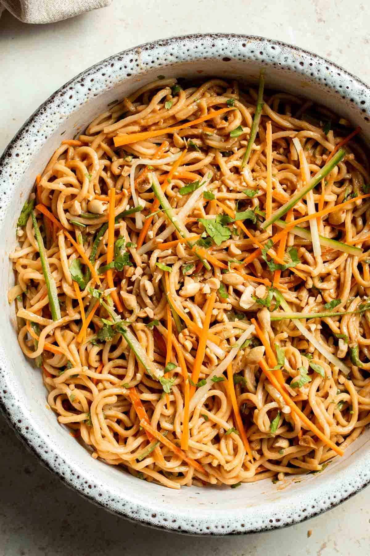 A bowl of noodles mixed with julienned carrots, cucumber, bean sprouts, chopped peanuts, and fresh cilantro, all tossed in a light sauce.