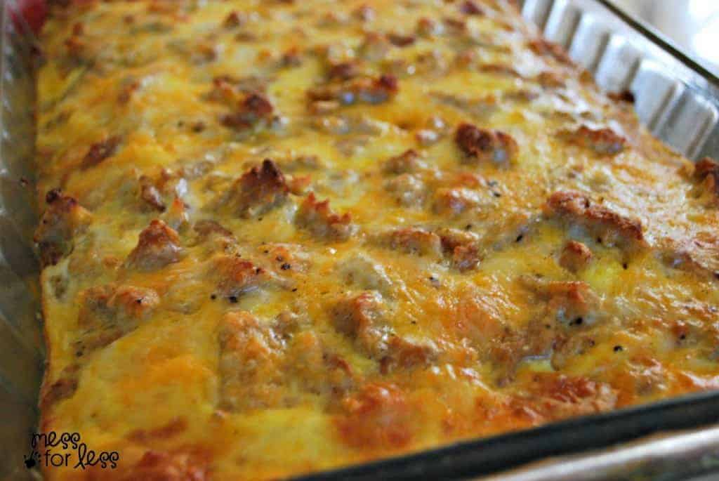 A close-up of a baked breakfast casserole in a glass dish, featuring a golden-brown, cheesy top with visible chunks of sausage and eggs.