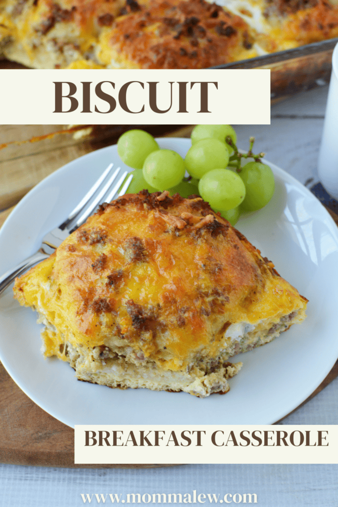 A plate featuring Biscuit Breakfast Casserole, topped with melted cheese, is served alongside fresh green grapes and a fork. The image displays the text: Biscuit Breakfast Casserole and www.mommalew.com.