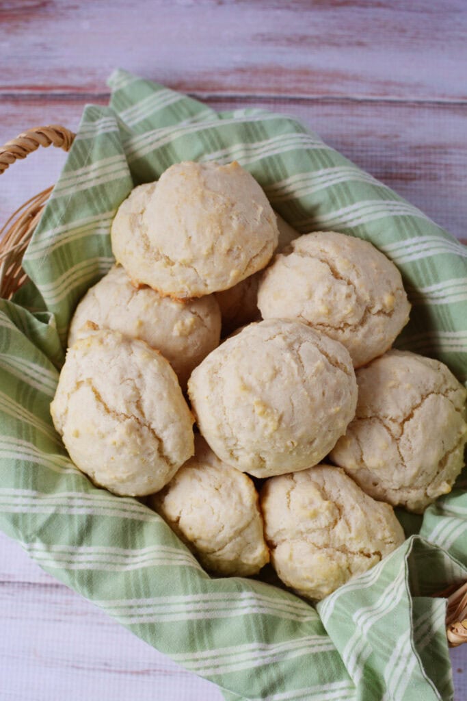 A basket lined with a green plaid cloth holds several round, golden homemade biscuits made from a classic drop biscuit recipe on a light wooden surface.