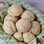 A basket lined with a green and white striped cloth, filled with round, golden-brown biscuits made from a classic Drop Biscuit Recipe, sits atop a light wooden surface.