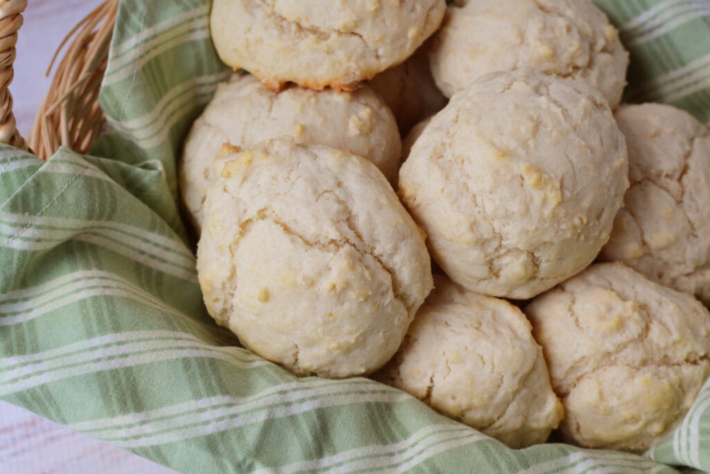 A basket lined with a green and white plaid cloth holds several homemade, golden-brown drop biscuits with a slightly cracked surface, made using a classic drop biscuit recipe.