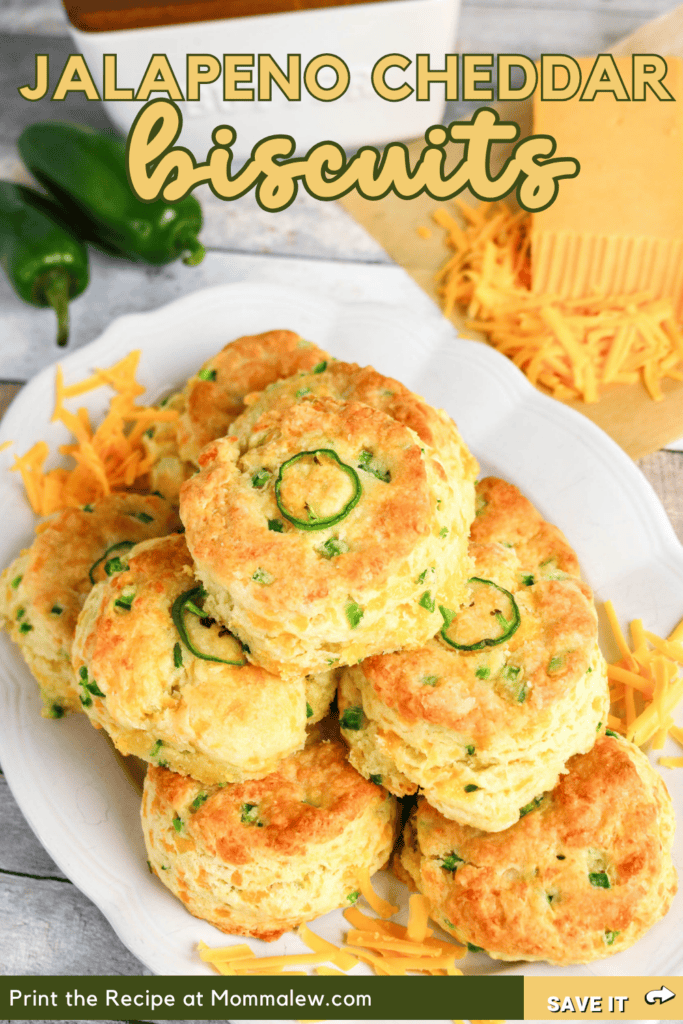 A plate of golden brown Jalapeno Cheddar Biscuits is stacked high, surrounded by sliced jalapeños and shredded cheddar cheese. The text reads Jalapeno Cheddar Biscuits.