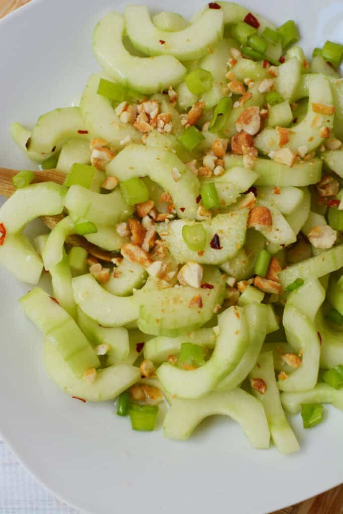 Thai cucumber salad on a white plate, topped with chopped green onions and crushed peanuts, with a light dressing visible.