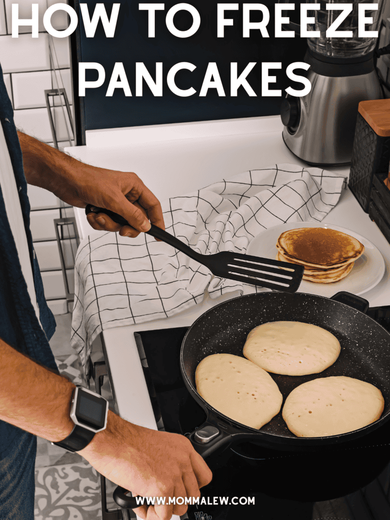 A person cooks pancakes on a stovetop using a spatula, with a stack of cooked pancakes on a plate. Text at the top reads, How to Freeze Pancakes. Website www.mommalew.com is at the bottom.