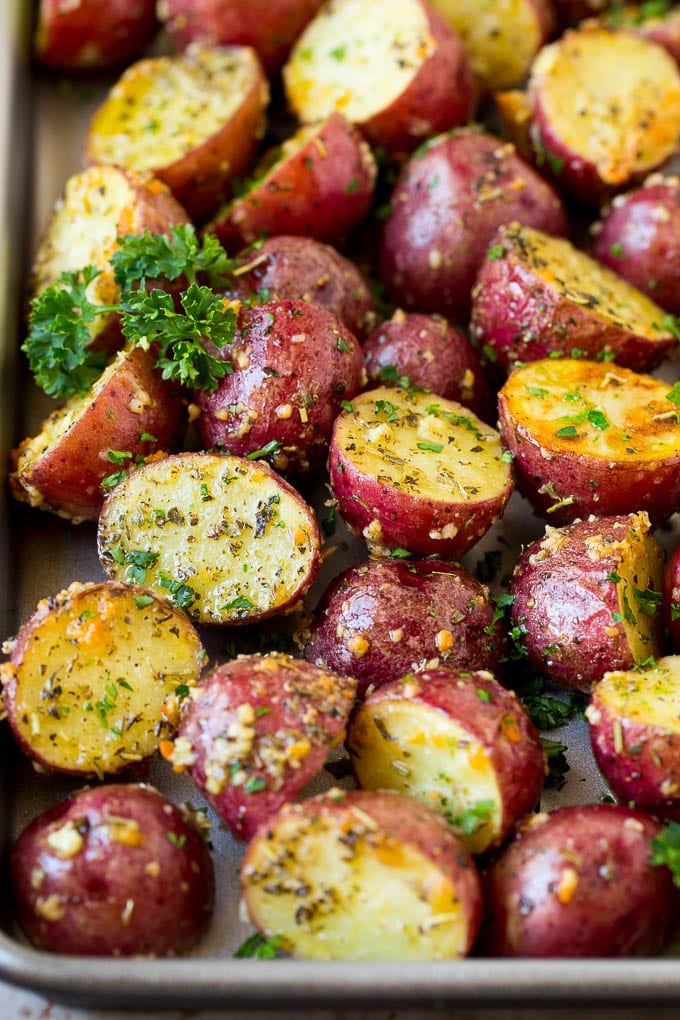 Roasted red potatoes, halved, seasoned with herbs and spices, garnished with chopped parsley, and arranged on a baking sheet.